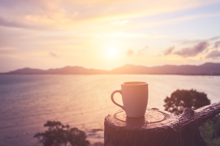 Close up coffee cup at sunset or sunrise beach in the with lens flare. Warm toning effect. Retro and vintage styleの写真素材