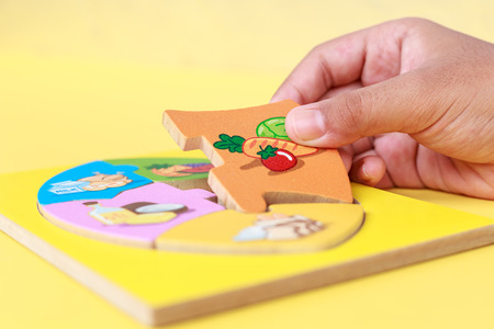 Close up hand of kid holding wooden jigsaw of the 5 food Groups. Child development conceptの写真素材