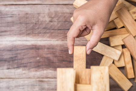 Close up hand holding blocks wood game   on wooden plank background. Risk conceptの写真素材
