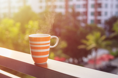 Close up orange coffee cup on balcony of hotel and blurred view of buildingの写真素材