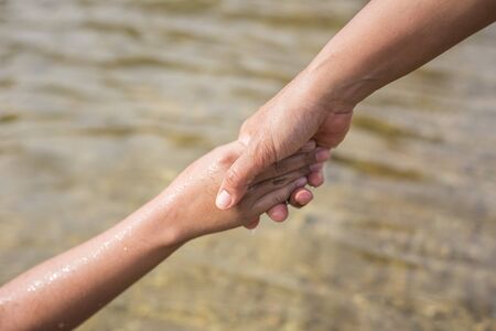 Close up woman holding her daughter hand in the river. Help concept