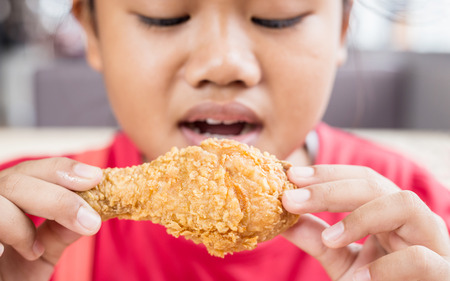 Asian children eating fried chicken in the restaurant. Focus on chickenの写真素材