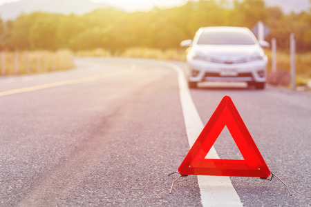 Red emergency stop sign and broken silver car on the roadの写真素材