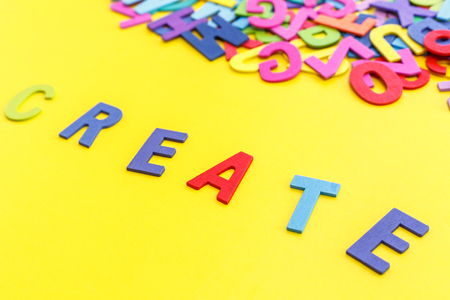 Colorful wooden alphabet and word "CREATE". Top view on yellow table backgroundの写真素材