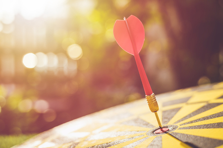 Close up red dart arrow in the center of dartboard. Blur and bokeh in sunrise time backgroundの写真素材