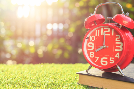 Close up red alarm clock on green grass with sunlight blur and bokeh background in morning timeの写真素材