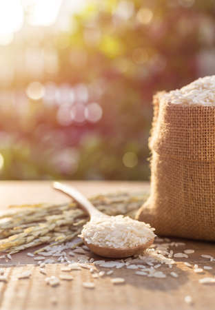 Close up Thai jasmine rice in small sack on wooden table with sunlight blur and bokeh background in morning timeの写真素材