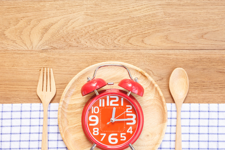 Top view red alarm clock in wooden dish, spoon and fork on wooden plank background. Time eating conceptの写真素材