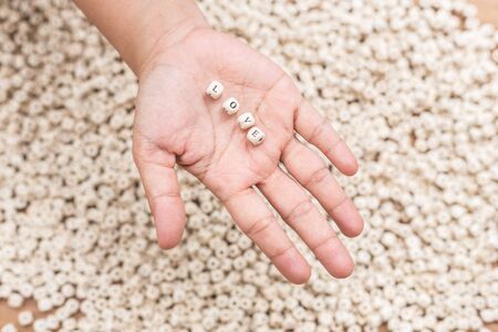 LOVE word in woman hand above pattern of white english alphabet letters on wooden plankの写真素材