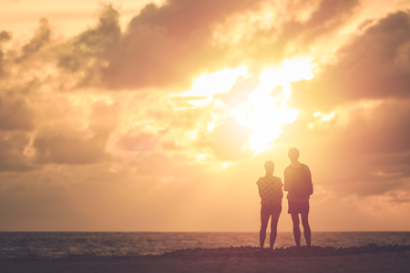 Silhouette of couple people or tourist standing on the tropical beach in sunset time. Warm tone and vintage filter effectの写真素材