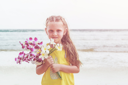 Caucasian little girl from europe holding orchid flower with happy and relax time on the tropical beach at Karon, Phuket province southern of Thailandの写真素材