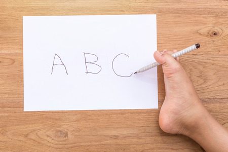 Word ABC in white paper writing by right foot of disabled people on wooden desk. Use for donation...