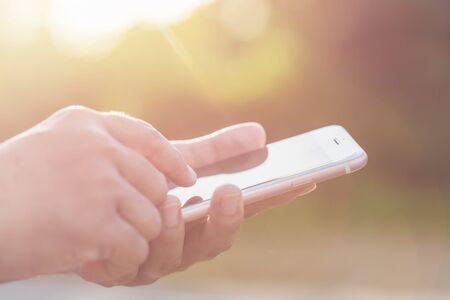 Close up hand of woman holding or using smartphone on green blur and sunlight effectの写真素材