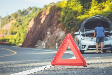 Asian woman using smartphone in front of her broken car on the road. Contacting car technician or need help conceptの写真素材