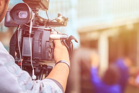 Cameraman using black professional digital video camera. Outdoor setup and working
