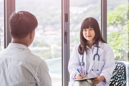 Portrait female doctor discussing with her male patient beside the windows at the hospital. For medical and health care conceptの写真素材