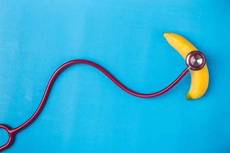 Close up Stethoscope and yellow banana on blue background. For men penis check up concept. With empty free space for text or design. Top viewの写真素材