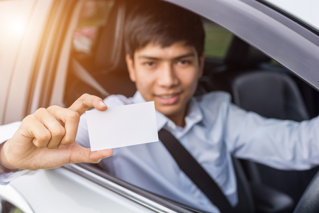 Young asian businessman sitting in the modern car and holding blank of white paper or business card. For car rent or car business conceptの写真素材
