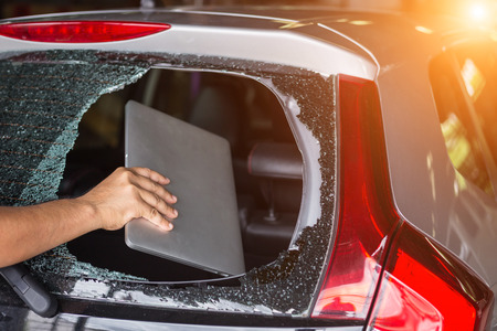 Close up hand stealing laptop from back side of car which rear glass brokenの写真素材