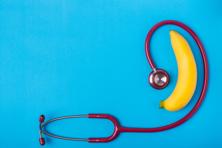 Close up Stethoscope and yellow banana on blue background. For men penis check up concept. With empty free space for text or design. Top viewの写真素材