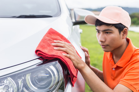Young asian man using red microfiber cloth cleaning body of new silver car. For car maintenance concept.の写真素材