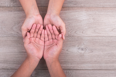 Help and support Concept : Woman holds her young kids hands on brown wooden table background. Free space for text or designの写真素材