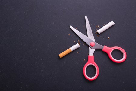 Stop smoking concept. Pink scissor cut cigarette in meaning STOP. Top view on black board backgroundの写真素材