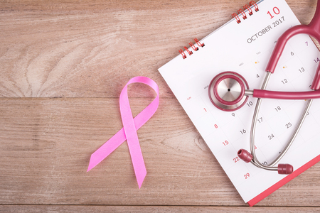 Breast Cancer concept : Pink ribbon symbol of breast cancer, calendar and stethoscope on brown wooden table background. For breast/body checking appointmentの写真素材