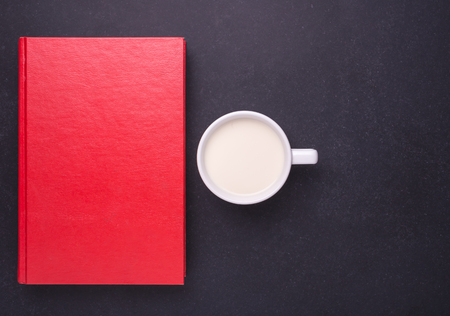 Milk in white glass and red book on black stone table background. Top view and Studio shotの写真素材