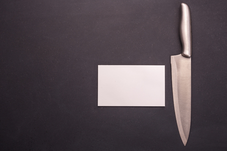 New stainless steel cooking knife on black stone background. Top view with free space and paper note for text or designの写真素材