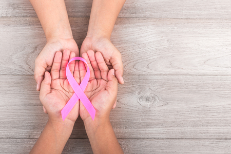Breast Cancer concept : Woman holds her young kids hands and supporting Pink ribbon symbol of breast cancer on brown wooden table background. Free space for text or designの写真素材