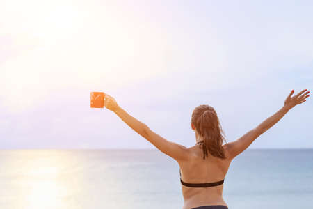 Caucasian woman drinking coffee in red cup and relax on the tropical beach in morning time. With...