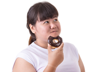 Fat asian woman wearing white t-shirt and eating donut isolated on white background. Food and Healthcare conceptの写真素材