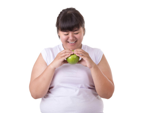 Fat asian woman wearing white t-shirt and eating green apple isolated on white background. Food and Healthcare conceptの写真素材