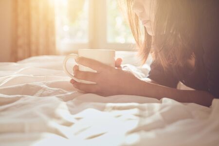 Close up asian woman holding coffee cup on the bed in morning time, focus on faceの写真素材