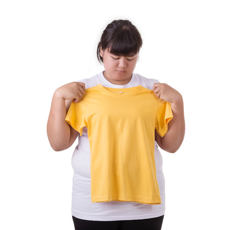 Fat asian woman trying to wear small size of yellow t-shirt isolated on white background. Fat and Healthcare conceptの写真素材