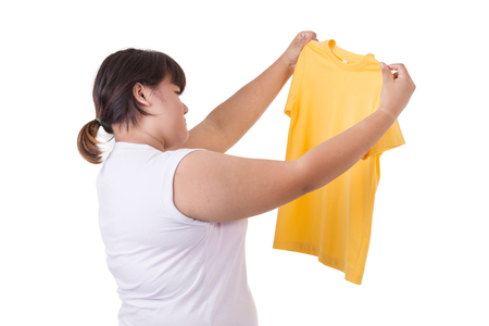 Fat asian woman trying to wear small size of yellow t-shirt isolated on white background. Fat and Healthcare conceptの写真素材
