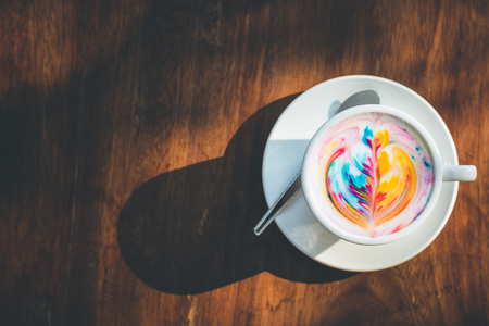 Top view of colorful rainbow latte coffee in white cup on wooden table with copy space for text or designの写真素材