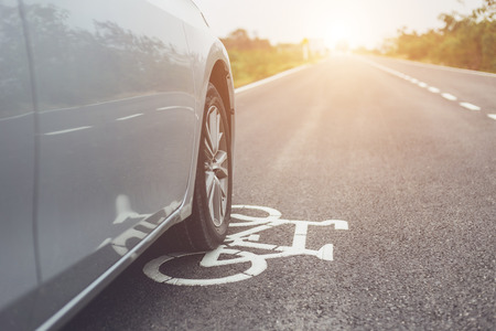 Front of modern car running on asphalt road / bicycle lane and tread on white bicycle signの写真素材