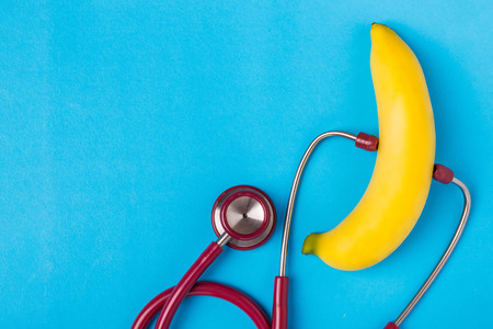 Close up Stethoscope and yellow banana on blue background. For men penis check up concept. With empty free space for text or design. Top viewの写真素材
