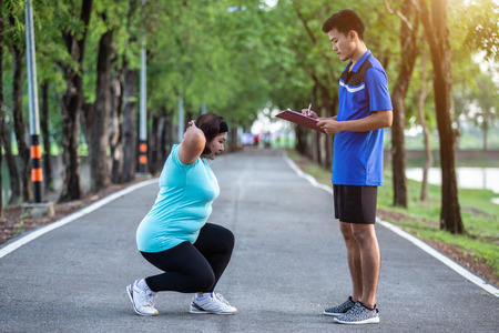 Asian man writing on paper in front of fat women while doing scot jump in the parkの写真素材