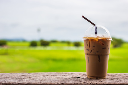 Close up iced coffee in plastic cup with drinking straw on terrace and green field backgroundの写真素材