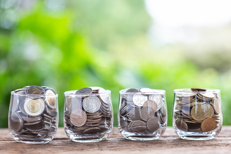 Close up coins in money jar on wooden plank with green blur background. savings concept.の写真素材