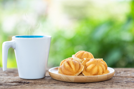 Close up white coffee cup and ancient egg cakes on wooden table with blur light bokeh backgroundの写真素材