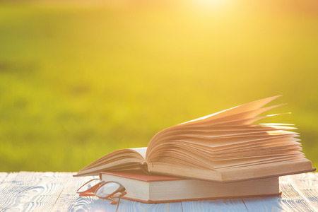 Close up book and eye glasses on wooden table with abstract blur and bokeh in sunrise or sunset timeの写真素材