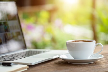 White ceramic coffee cup on wooden table or counter with morning nature light in garden conceptの写真素材