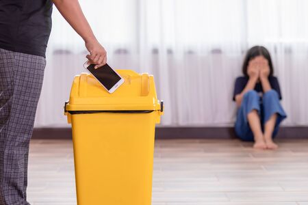 Mother punishing her daughter with throwing smartphone into yellow trash. Daughter used smartphone too muchの写真素材