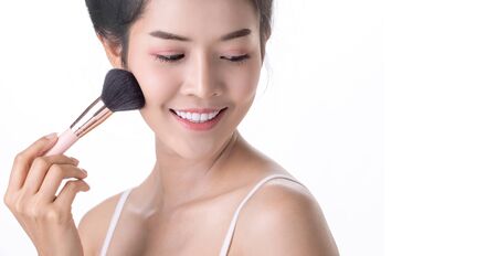 Beautiful Young Asian Woman using Soft Brush and Cosmetic on own face. Cosmetologist, Skin care or Beauty concept. Studio shot and isolated on White backgroundの写真素材