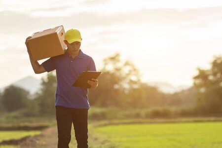 Delivery man holding brown parcel or cardboard boxes and delivery to customer at countryside and view of rice field. Can be delivery to anywhere conceptの写真素材