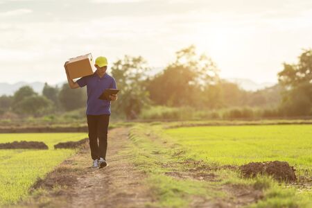 Delivery man holding brown parcel or cardboard boxes and delivery to customer at countryside and view of rice field. Can be delivery to anywhere conceptの写真素材
